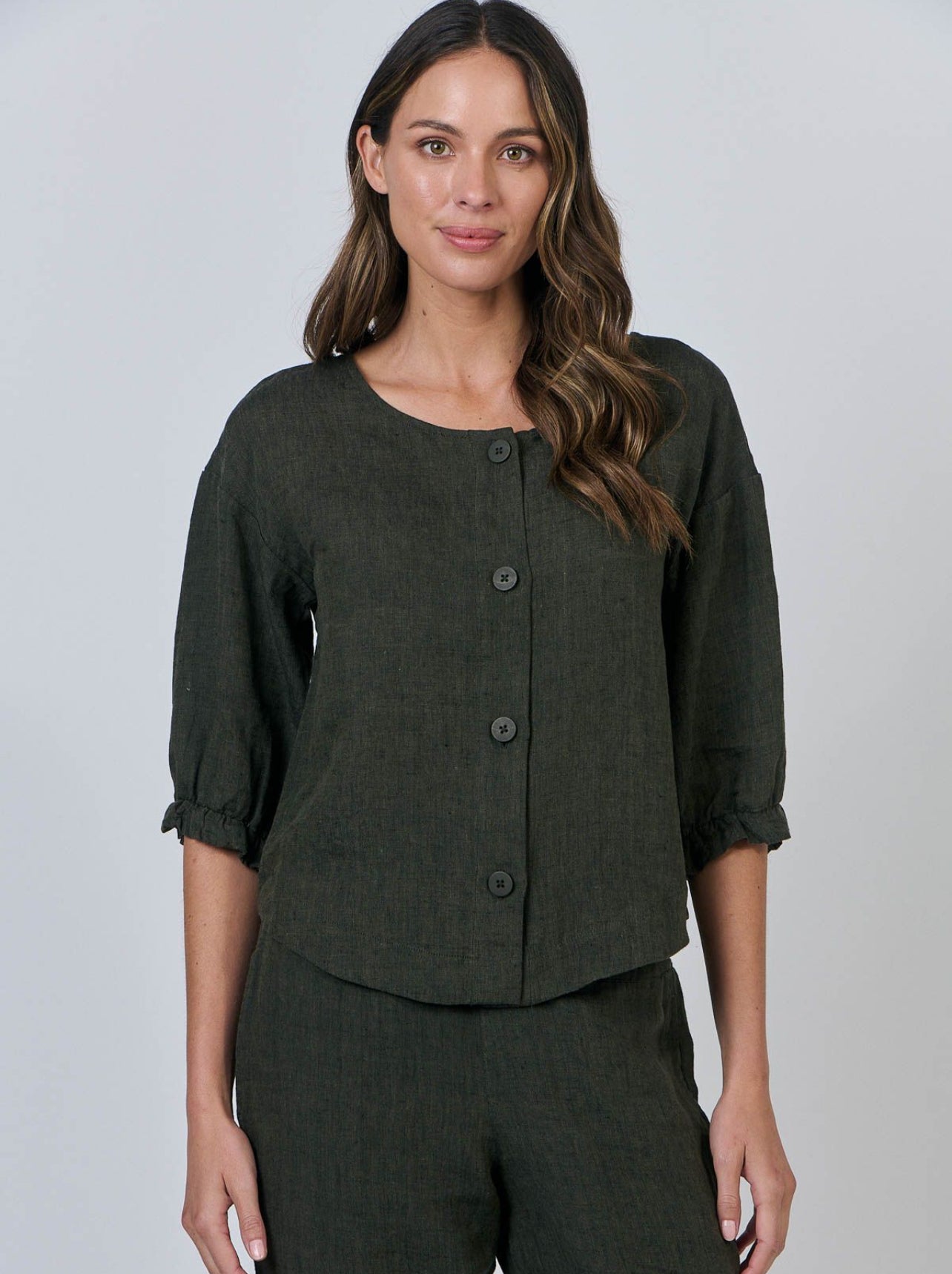 Woman wearing a dark green button-up top and pants against a plain background
